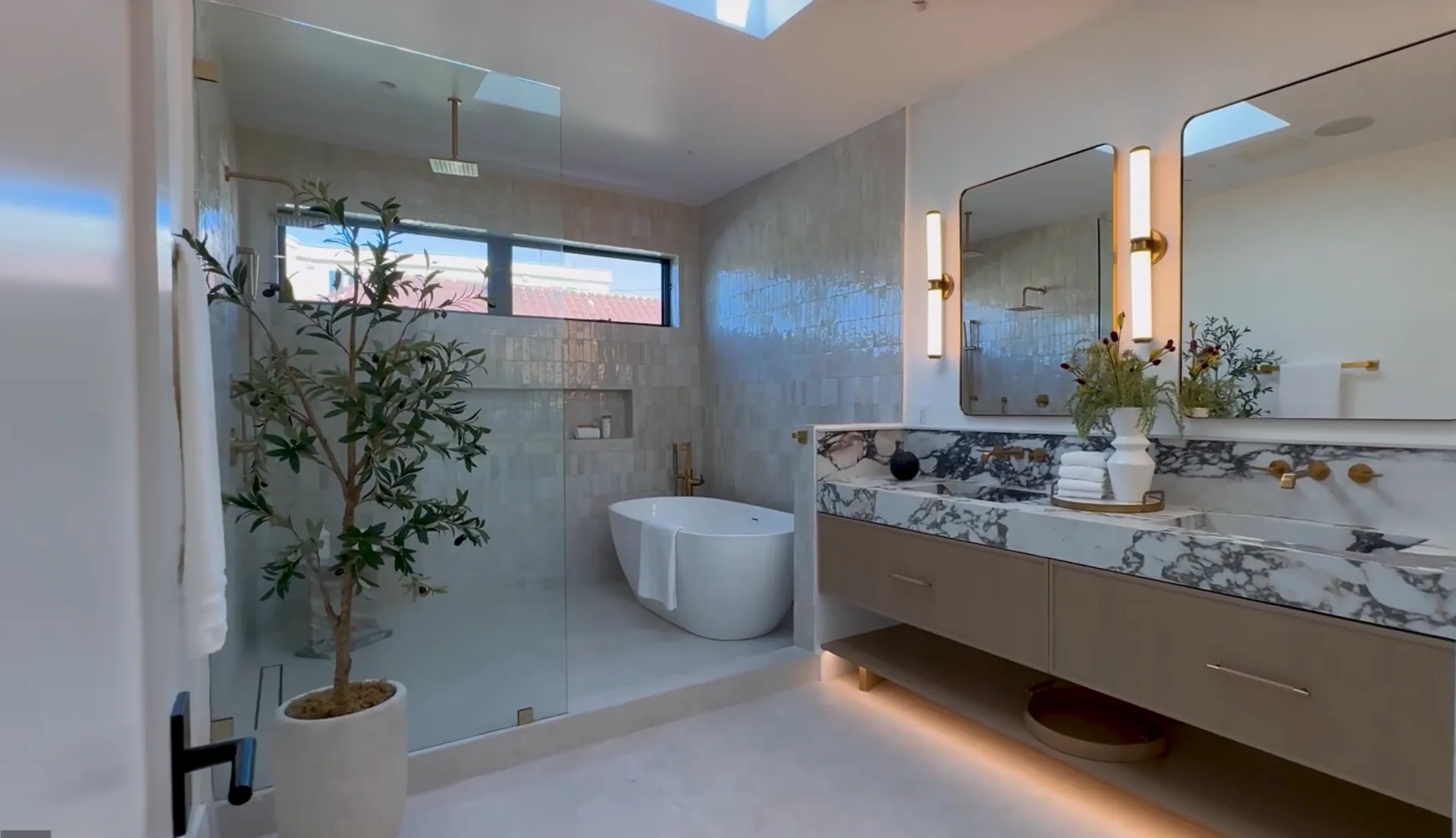 A luxury bathroom with glass shower, freestanding tub, marble vanity, and warm lighting
